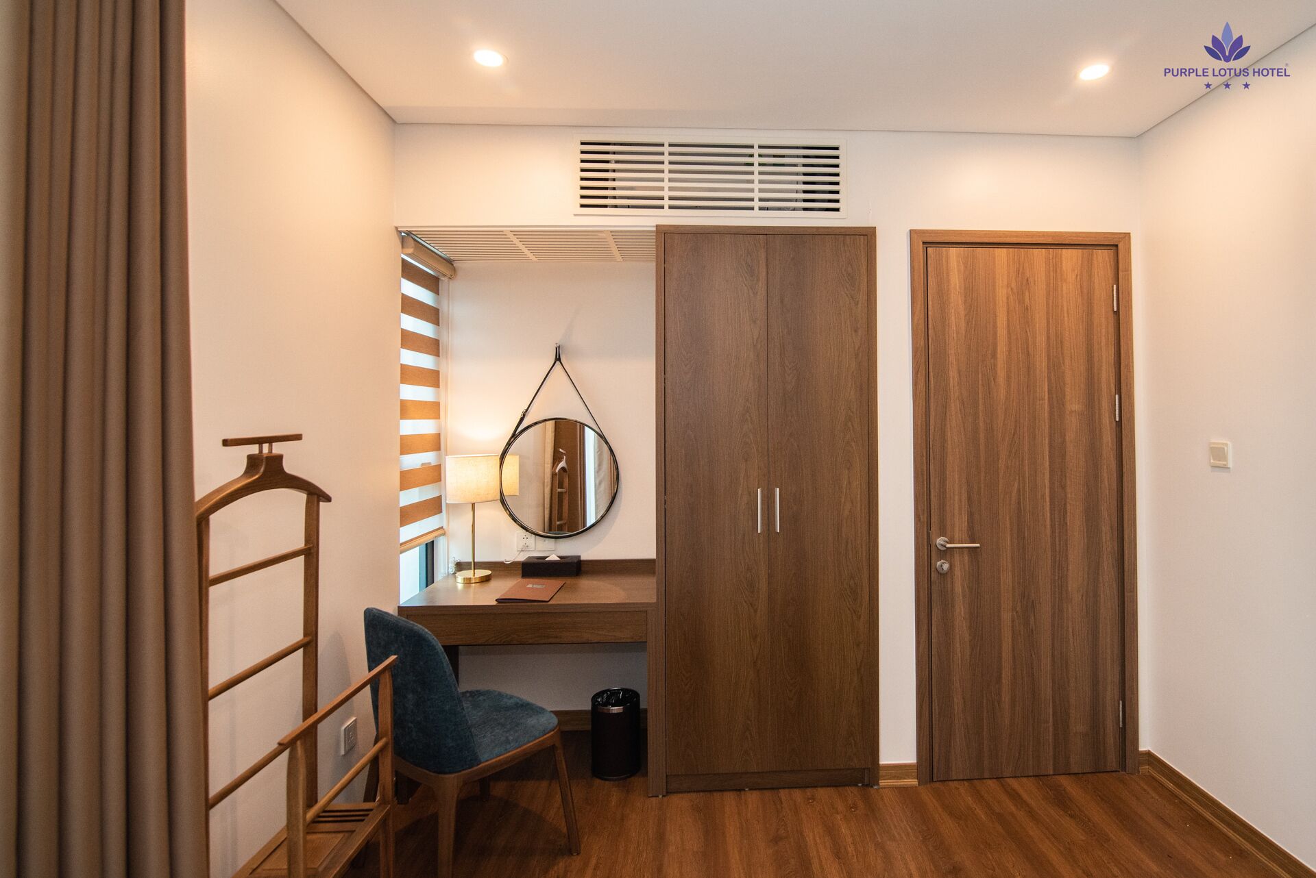 Habitación de hotel pequeña con un armario de madera, un escritorio con silla, un espejo colgado y un radiador.