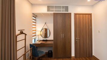 Habitación de hotel pequeña con un armario de madera, un escritorio con silla, un espejo colgado y un radiador.