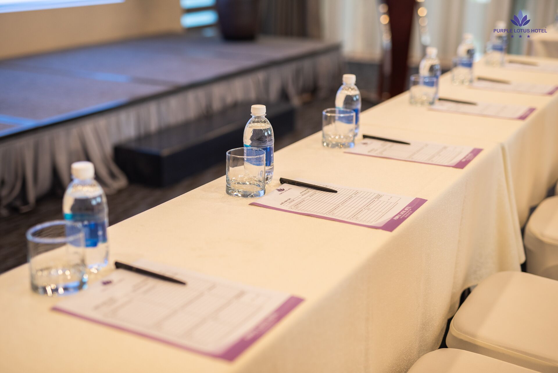 A conference room with tables set up for a meeting, each with a water bottle, glass, and notepad.