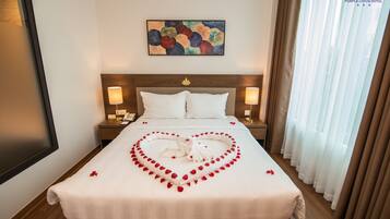 A hotel room with a bed, two bedside tables, a painting, and a window with curtains.