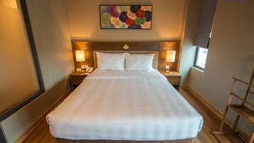 A large, neatly made bed with white linens in a hotel room. There are two bedside tables with lamps, a wall-mounted painting above the bed, and a window on the right side.