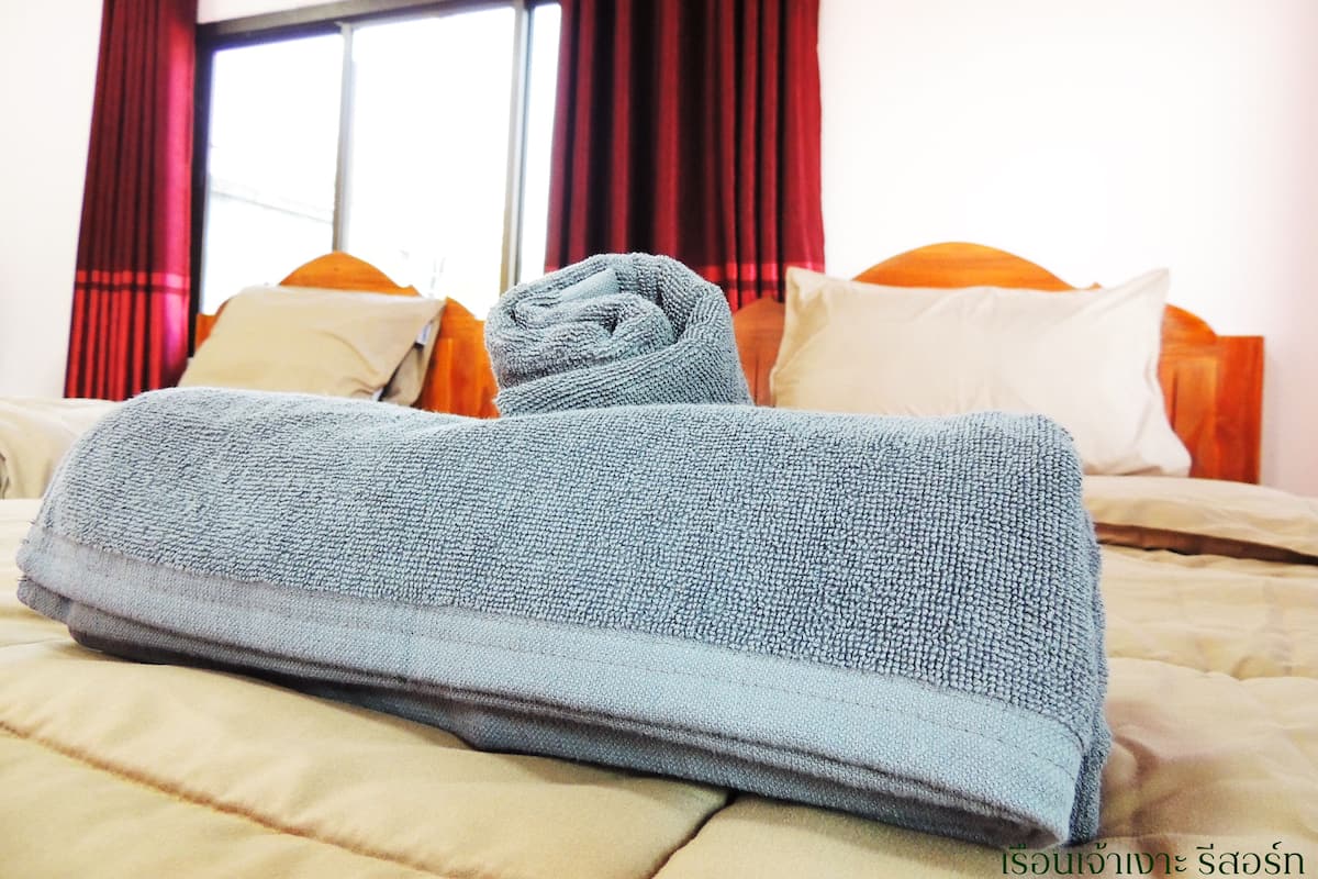 A neatly made bed with a folded towel, red curtains, and a window in the background.