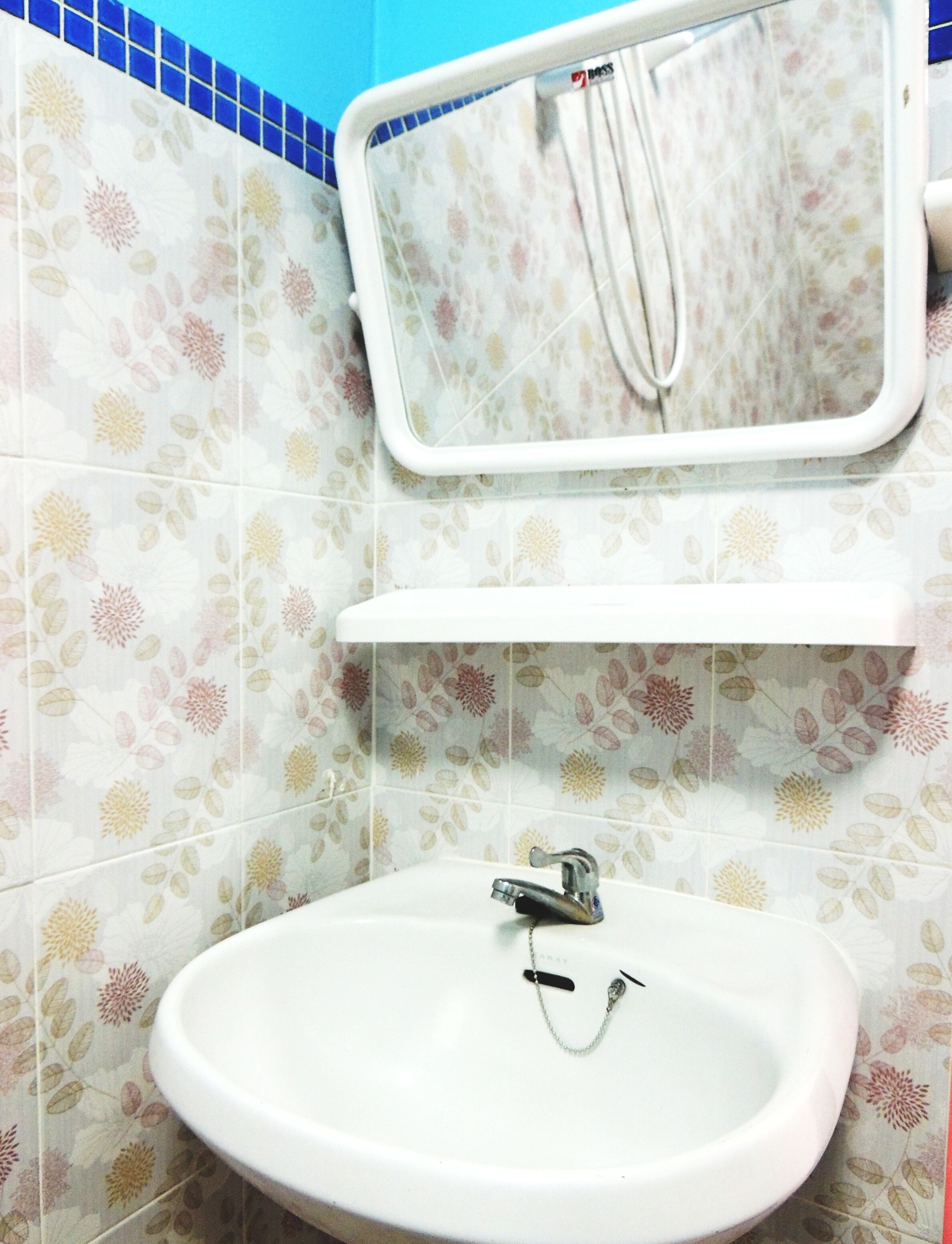A bathroom with a white sink, a mirror, and floral patterned tiles.