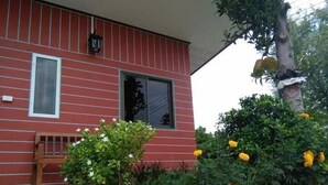 A red building with a bench and a small garden with yellow flowers. - Reuan Jao Ngao Resort (Maha Rat)