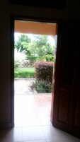 Una puerta abierta que da a un jardín exterior con suelo de baldosas y marco de madera.