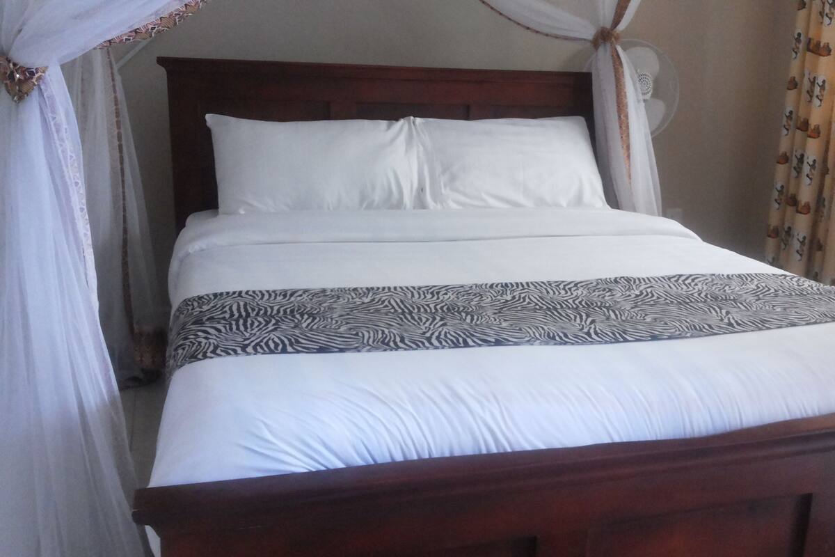 A bed with white bedding and a zebra-patterned accent, a wooden headboard, and sheer curtains with a decorative border.