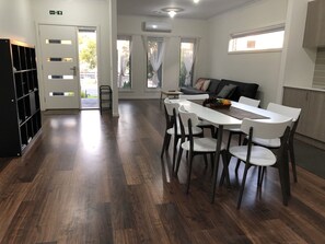 Un comedor moderno con una mesa y sillas blancas, una estantería negra y un sofá al fondo.