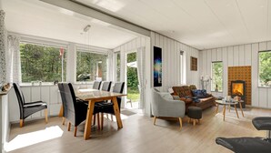 Ein geräumiges Wohnzimmer mit Essbereich, großen Fenstern, einem Kamin und Blick ins Grüne.