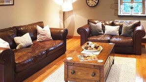 A living room with two brown leather sofas, a wooden coffee table with magazines, a wall clock, and a window with a view. - 3 bedroom accommodation in Hebden, near Grassington (Hebden, near Grassington)