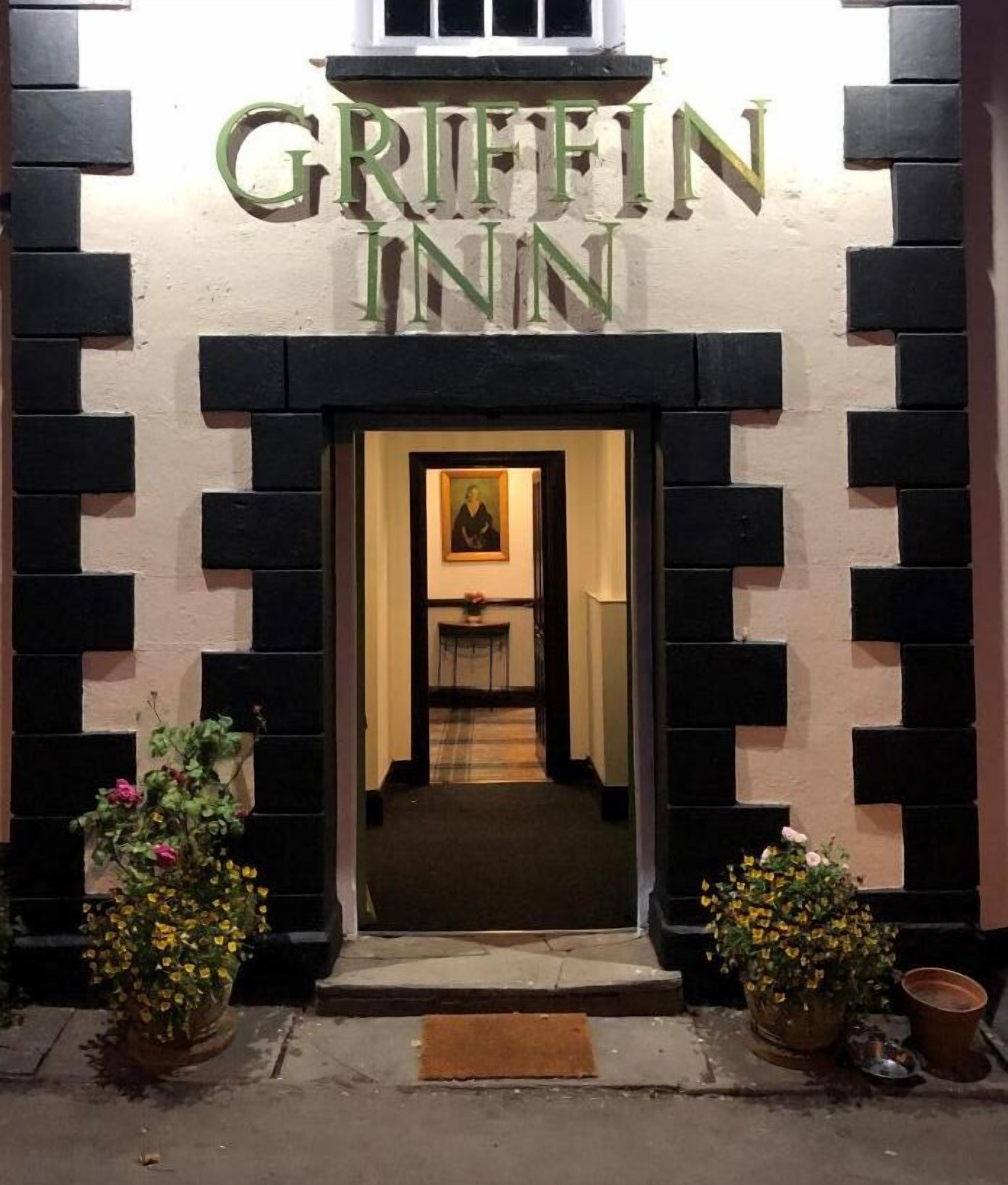 The Griffin Inn entrance with a black and white brick facade, a framed painting above the door, and potted plants on either side.