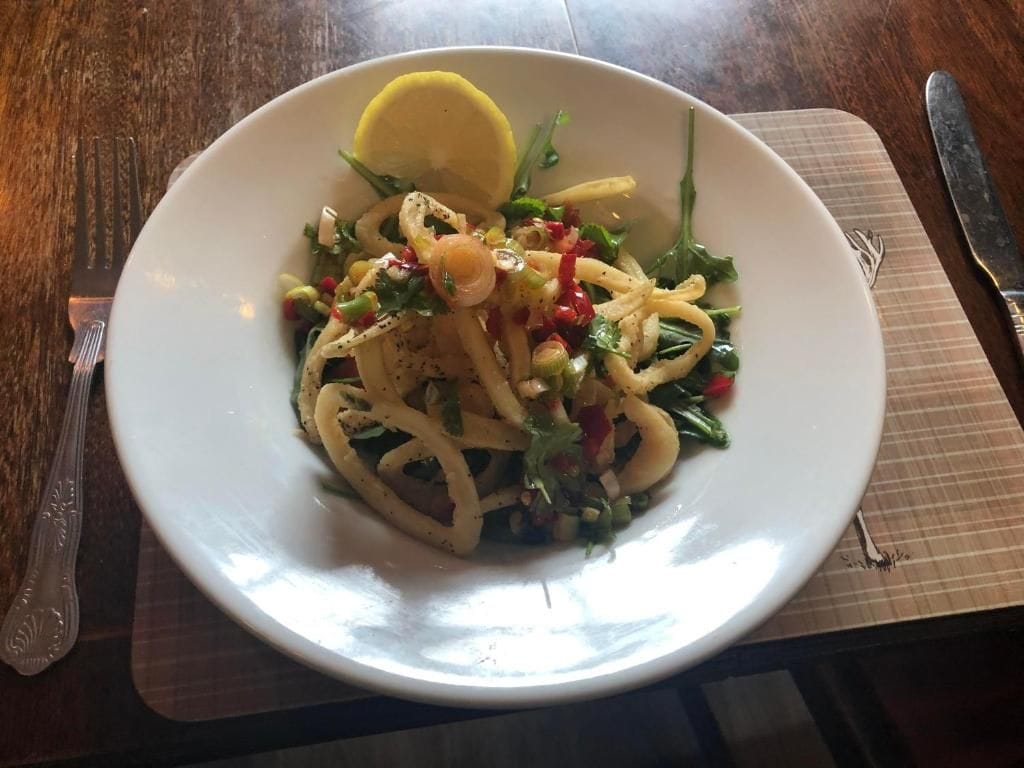 Un plato de pasta con verduras y un gajo de limón sobre un mantel individual.