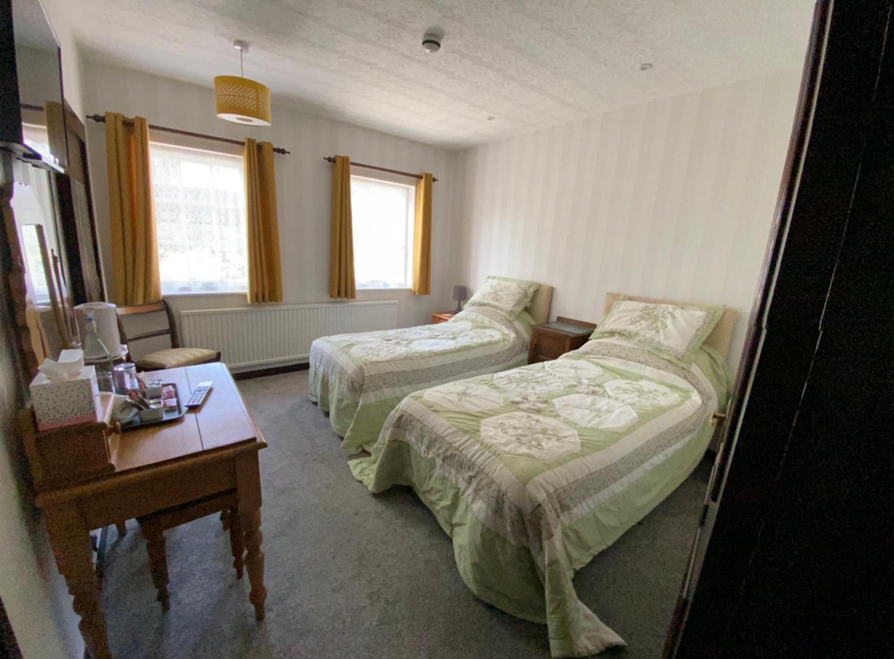 Ein Hotelzimmer mit zwei Einzelbetten, einem Holztisch mit Stuhl, einem Tisch mit Taschentuchbox und einer Lampe.