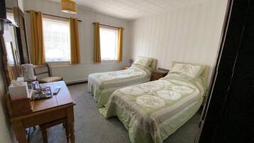 Une chambre d’hôtel avec deux lits simples, un bureau en bois avec une chaise, une table avec une boîte de mouchoirs et une lampe.