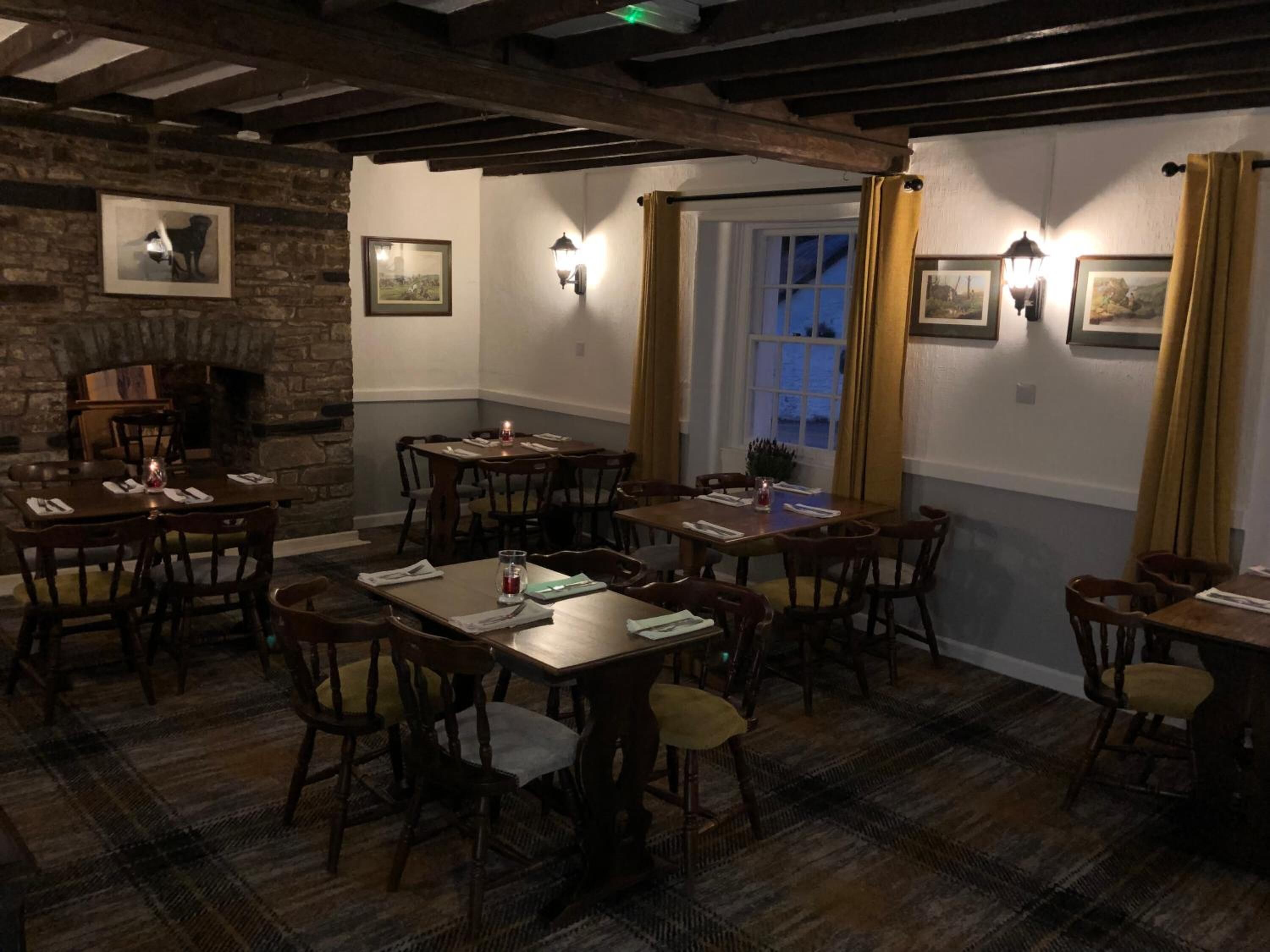 A cozy dining area with wooden tables and chairs, a fireplace, and framed pictures on the walls.