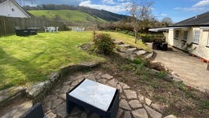 A backyard with a stone patio, a grassy lawn, and a white building with a sloped roof. - The Griffin Inn (Brecon)