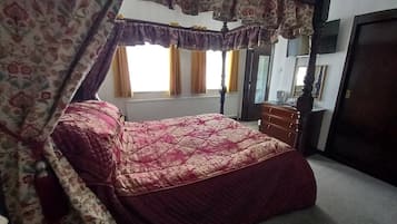 A bedroom with a four-poster bed, a wooden dresser, and a mirror on the wall.