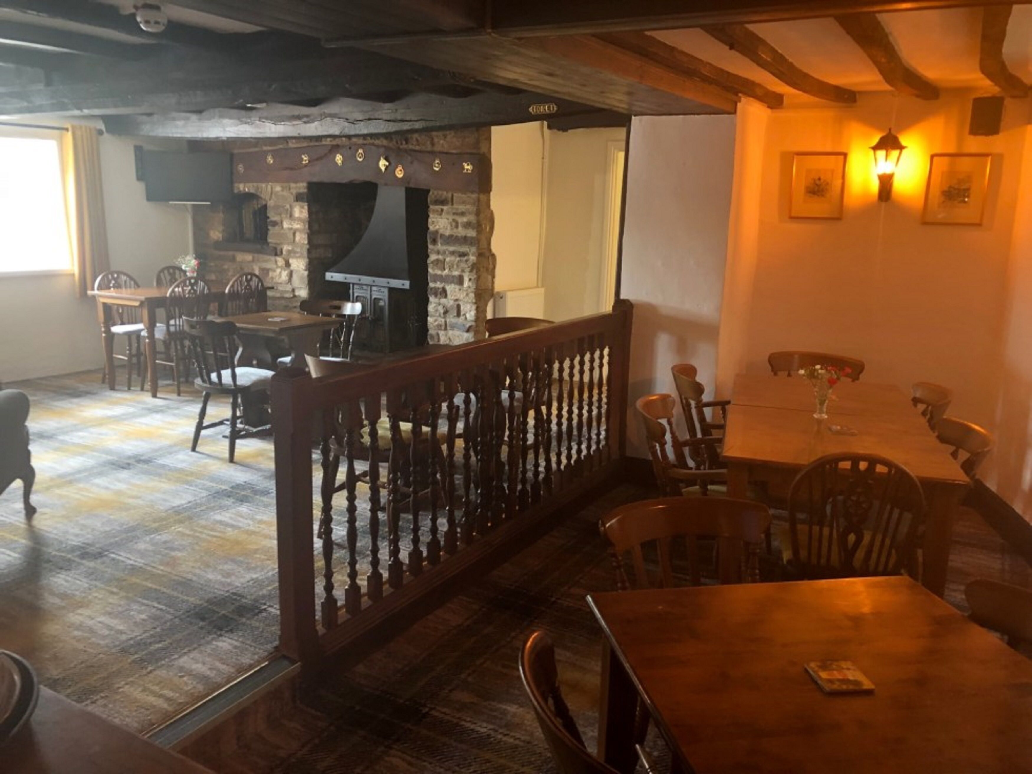 A rustic dining area with wooden tables and chairs, a brick fireplace, and a wooden railing.