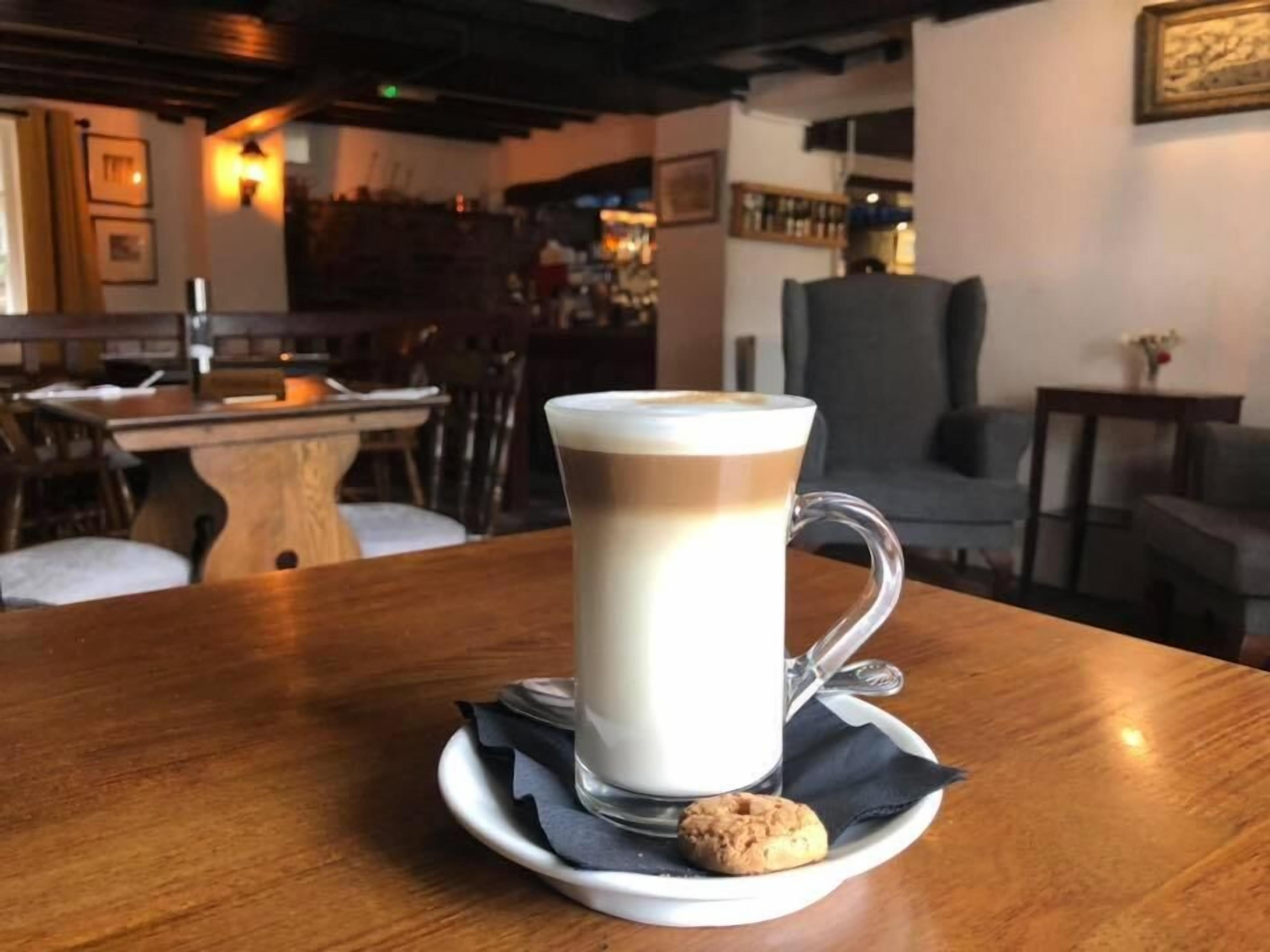 Une tasse de café posée sur une soucoupe, avec un biscuit sur une serviette, le tout placé sur une table en bois dans un café.