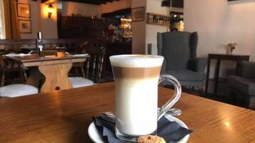 A cup of coffee on a saucer with a biscuit on a napkin, placed on a wooden table in a cafe setting.