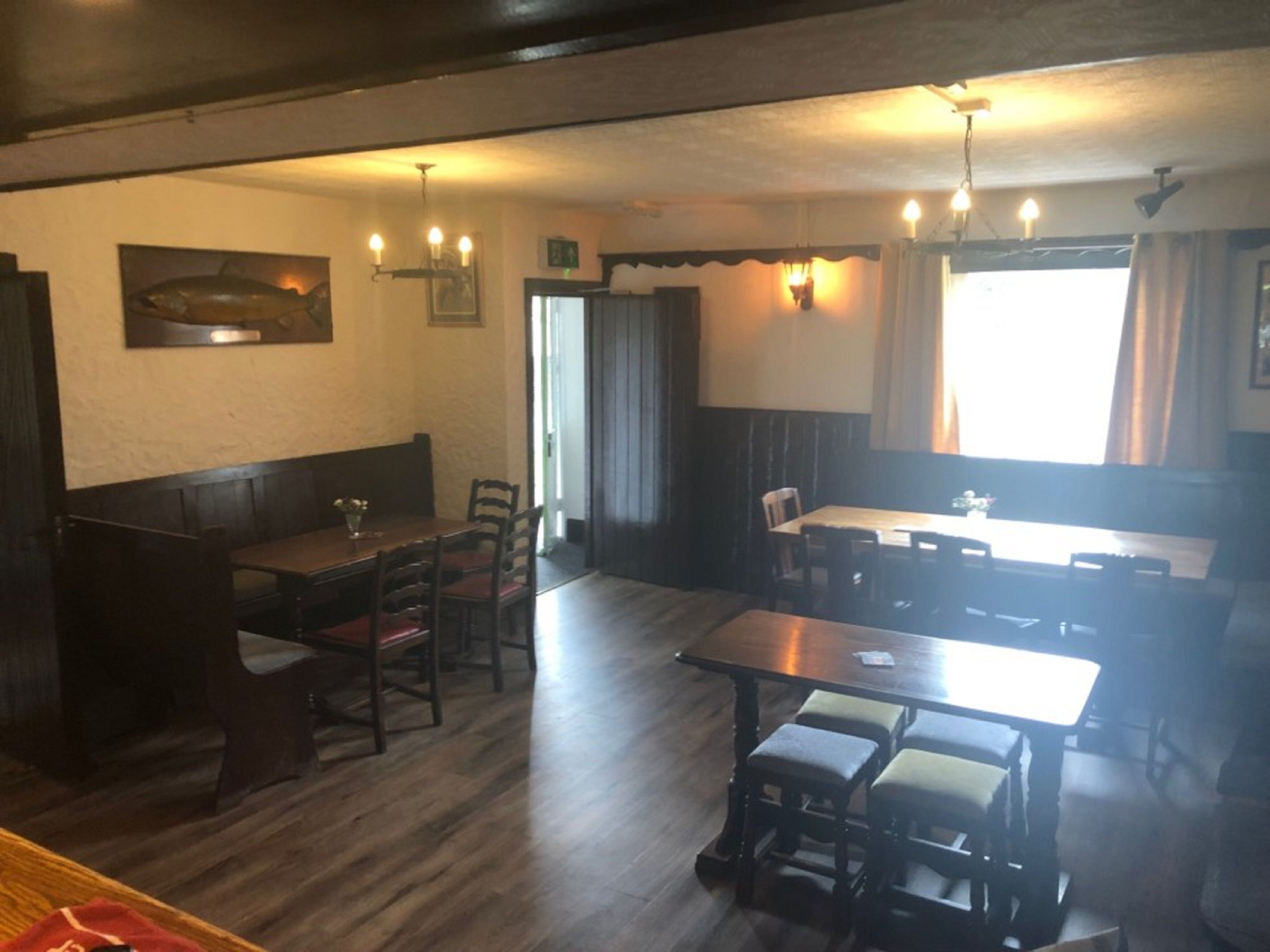 A restaurant with wooden tables and chairs, a fish mural on the wall, and a large window with curtains.
