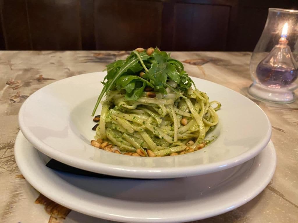Un plato de pasta con vegetales verdes y piñones sobre una mesa.