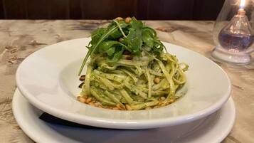 A plate of pasta with greens and pine nuts on a table.