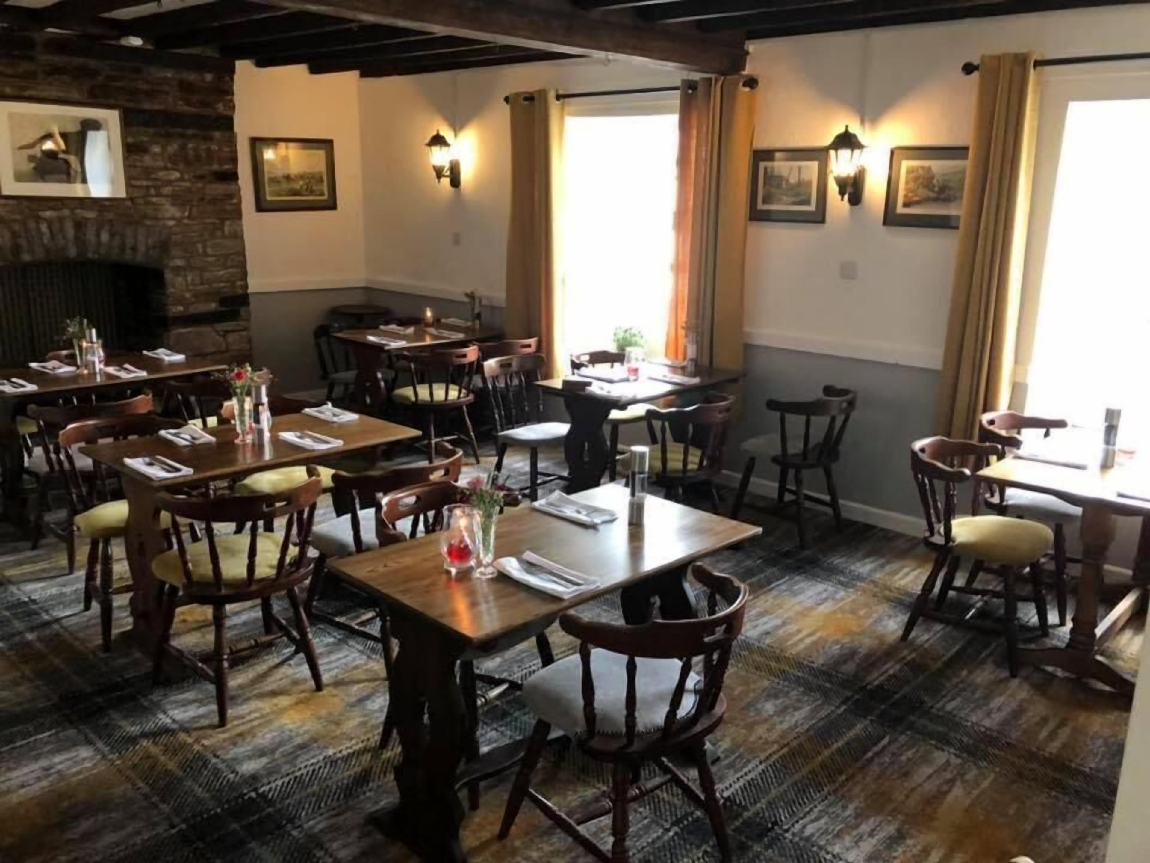 Un restaurante con mesas y sillas de madera, una pared de piedra y luces fijadas a la pared.