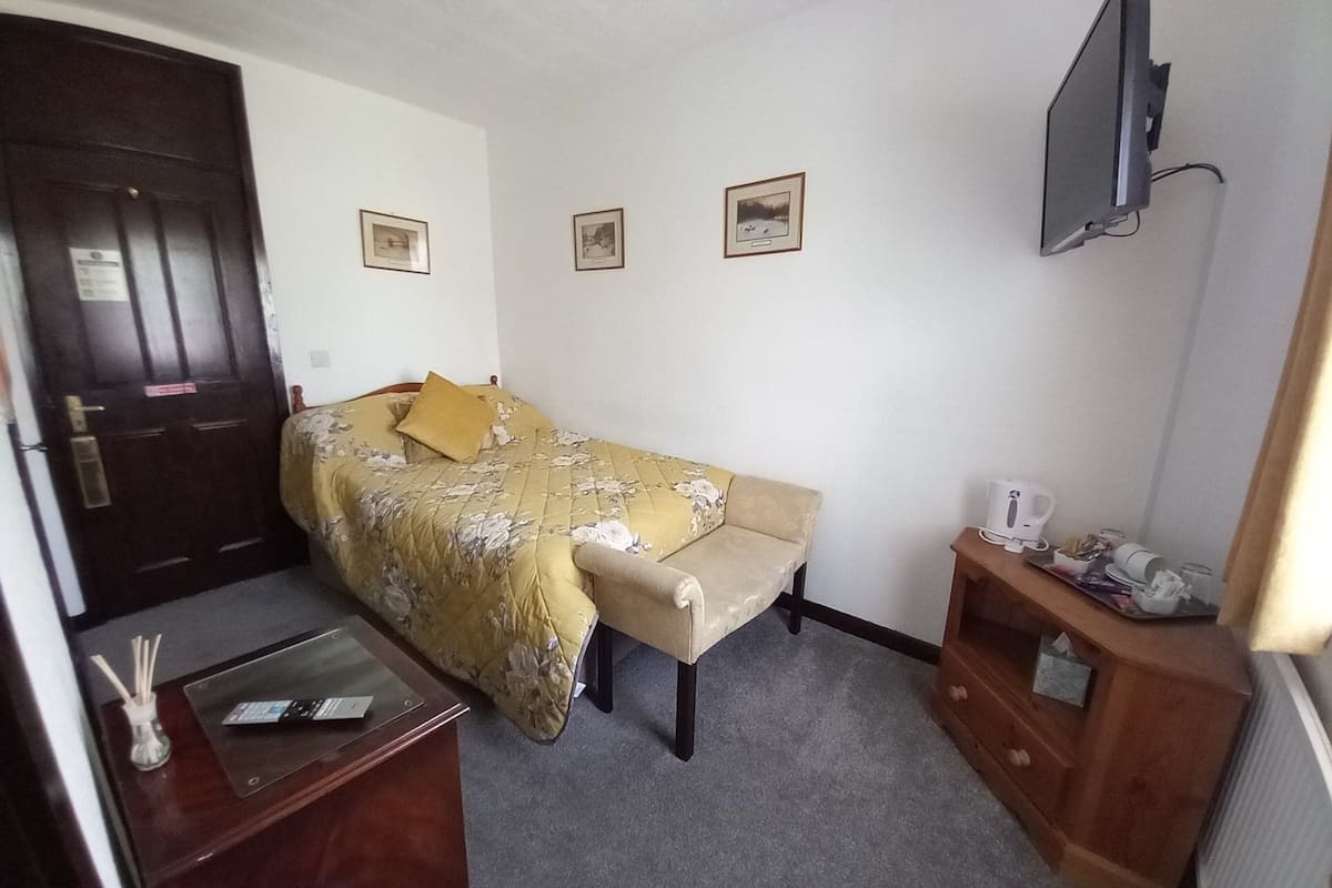 Um quarto pequeno e bem arrumado, com cama, escrivaninha, cadeira, televisão e porta.