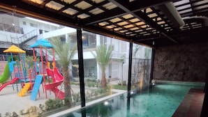 Une piscine intérieure dotée d’un espace de jeux pour enfants et d’un mur en pierre.