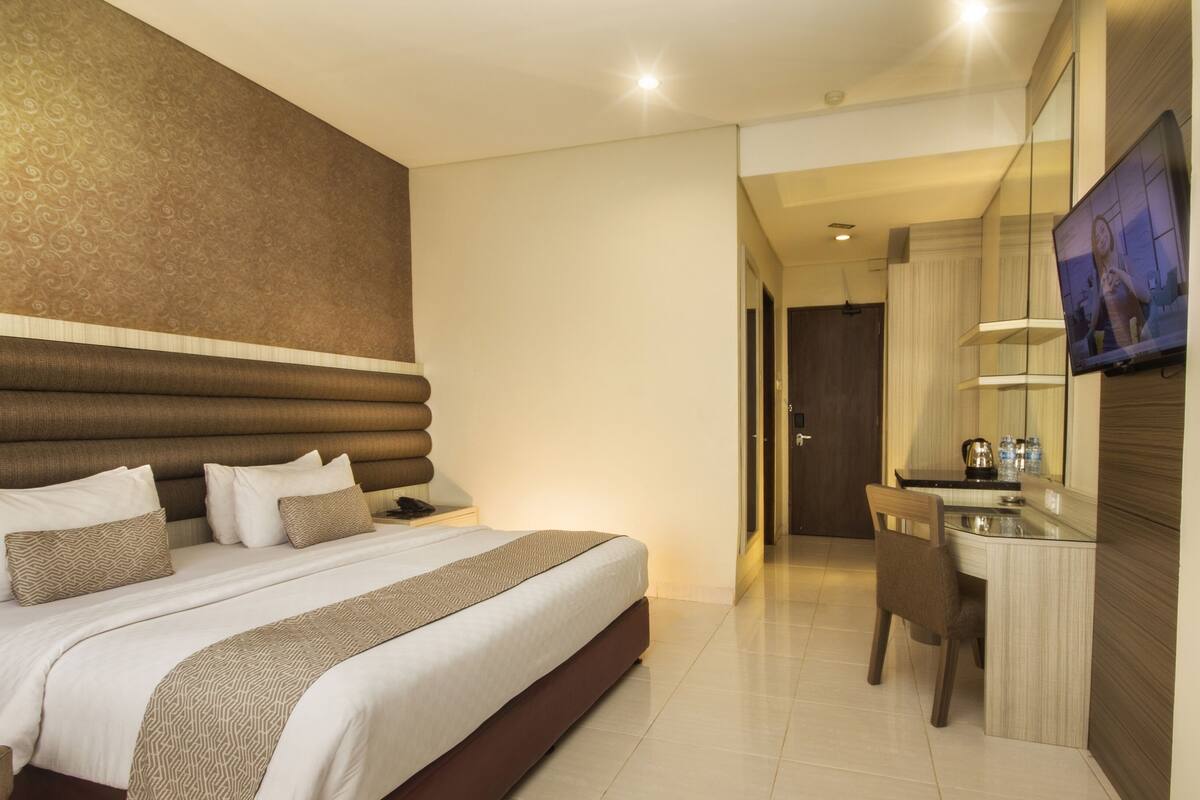 Une chambre d’hôtel avec un grand lit, une table de chevet, un bureau et un téléviseur.