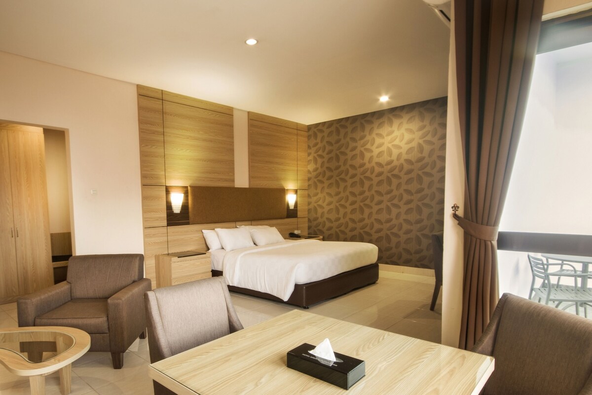 Une chambre d’hôtel comprenant un lit, deux fauteuils, une petite table et une table de chevet.