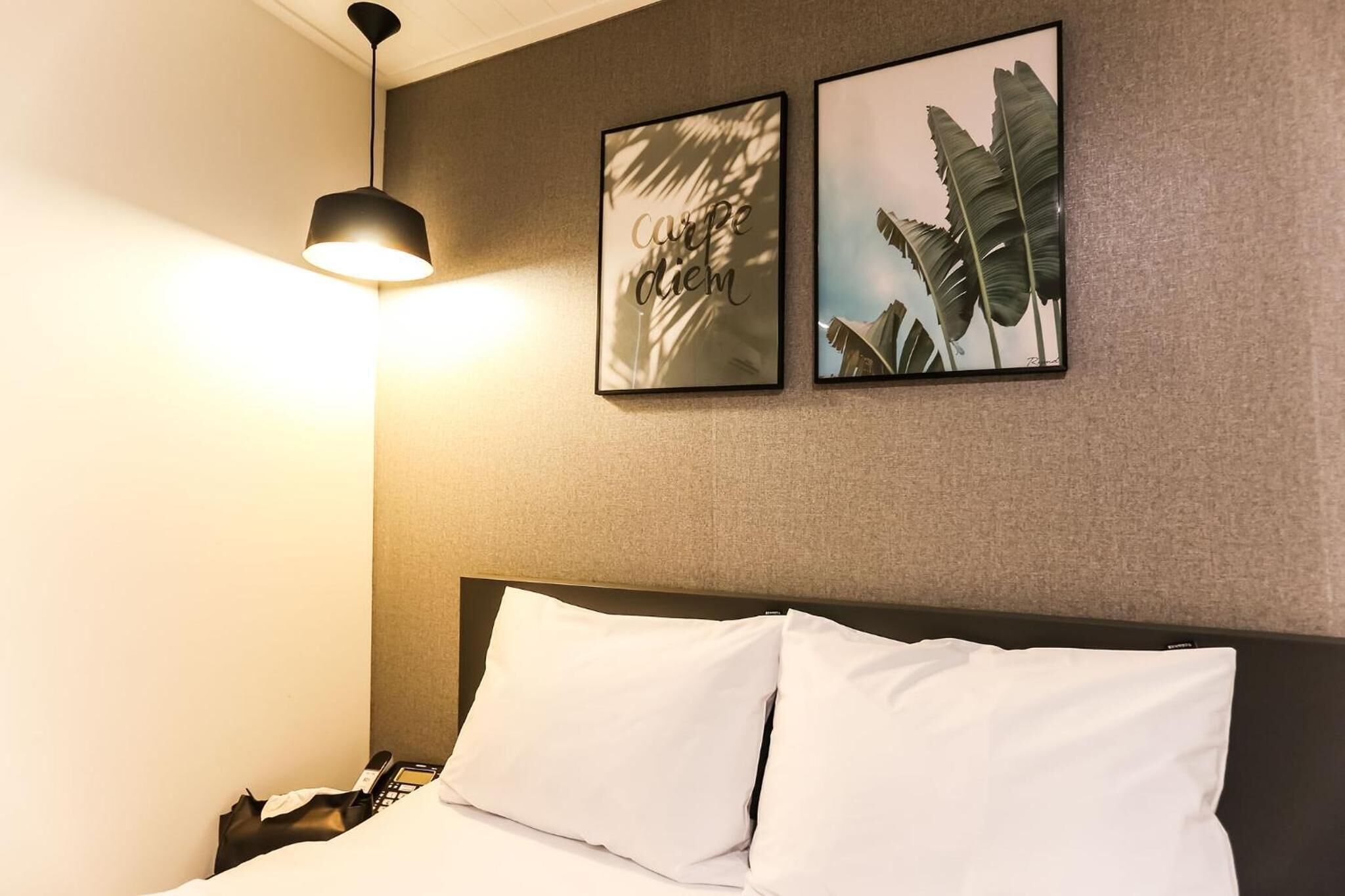 A hotel room with a bed, a black lamp, and two framed pictures on the wall.