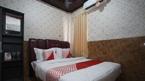 Une chambre d’hôtel comprenant un lit, une armoire, une étagère avec des articles de toilette et une fenêtre avec des rideaux.