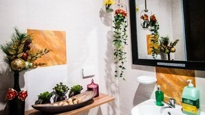 A bathroom with a white sink, a mirror, and a shelf with decorative items. - Downtown Suites (Cagayan de Oro)