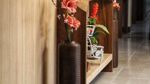 A reception area with a wooden reception desk, a vase with flowers, and a small potted plant. - Downtown Suites (Cagayan de Oro)