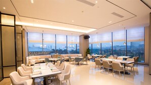 A modern dining area with tables and chairs, large windows with a city view, and a high ceiling with recessed lighting. - New Century Life Hotel Changchun (Changchun)