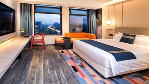 A hotel room with a bed, a desk, a chair, a sofa, and a view of the cityscape. - New Century Life Hotel Changchun (Changchun)