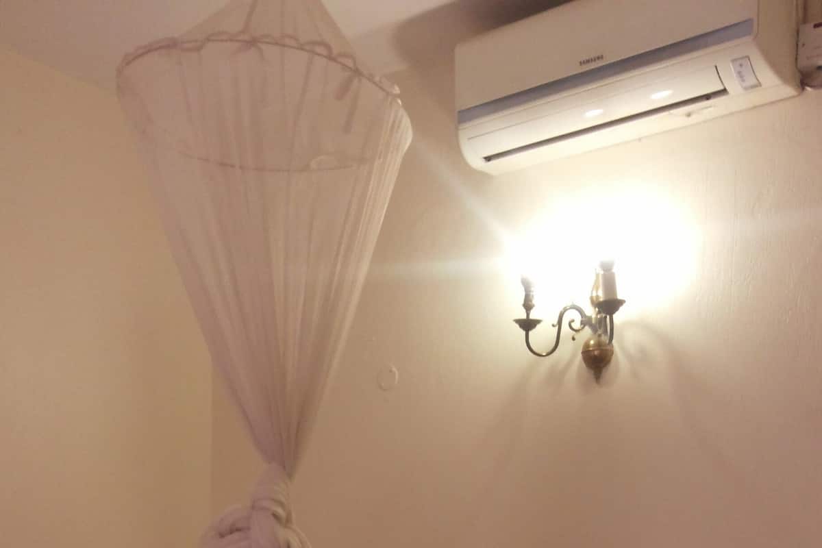 A bedroom with a bed, a mosquito net, an air conditioner, and a wall-mounted light fixture.
