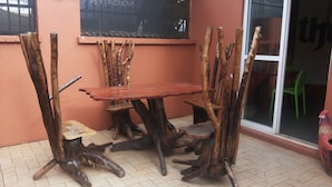 Una mesa de madera rústica con sillas hechas de ramas de árbol, frente a una pared color melocotón con una ventana y una puerta.