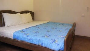 Una cama individual con estructura de madera, ropa de cama blanca y una colcha azul estampada con flores.