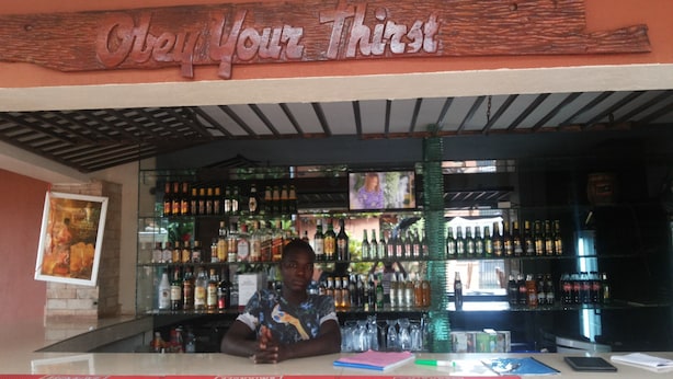 A bar with a wooden sign reading "Welcome Thirsty". There are shelves stocked with various bottles and glasses.