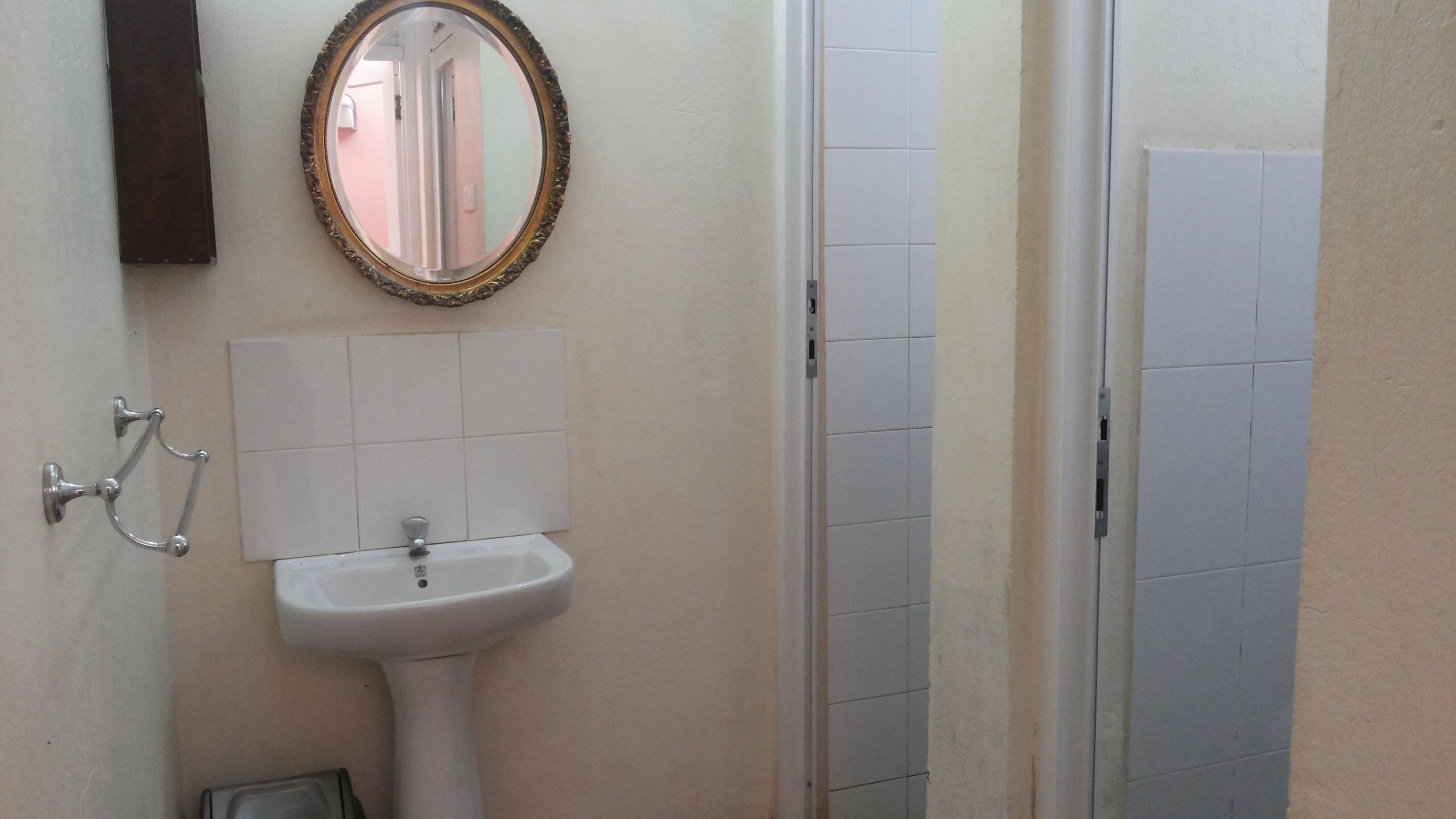 A bathroom with a white sink, a mirror with a decorative frame, and a door with a light switch.