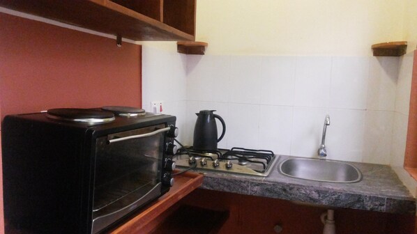 A compact kitchen with a stove, a kettle, and a sink.