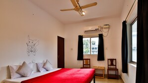 Quarto com cama, ventoinha no teto, ar condicionado, janela com cortinas e um adesivo de parede.