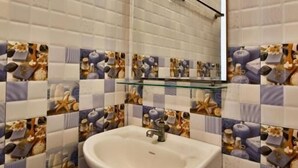 Casa de banho com lavatório branco, prateleira de vidro e espelho. As paredes são revestidas com azulejos em padrão azul e branco.