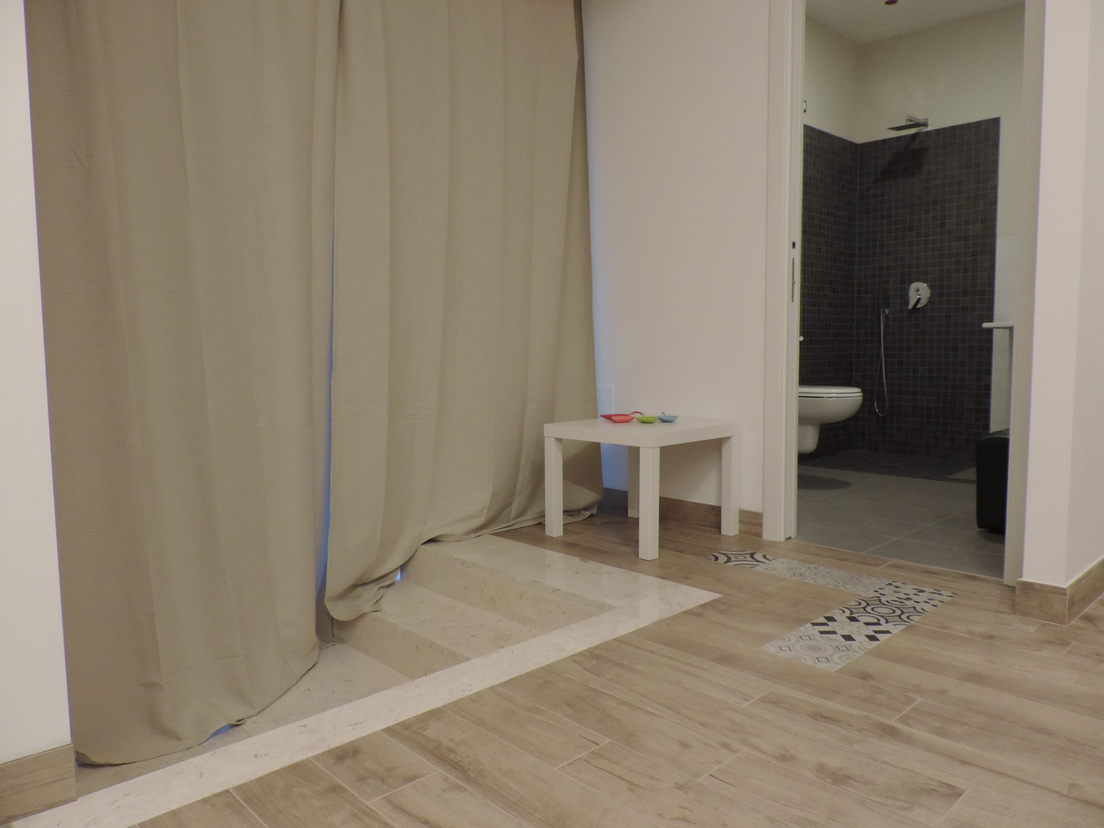 Et badeværelse med bruser, toilet og et lille bord med farverige skåle.