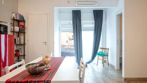 A dining area with a table set for two, a red refrigerator, a bookshelf, and a view through a doorway.