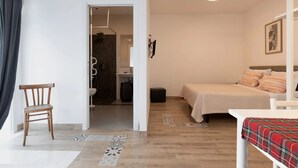 A bedroom with a bed, a chair, a small table, and a bathroom visible through an open door.