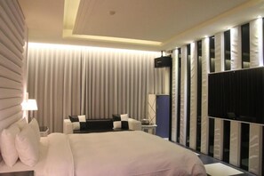 Une chambre d’hôtel avec un grand lit, un coin salon avec une table et un téléviseur fixé au mur.