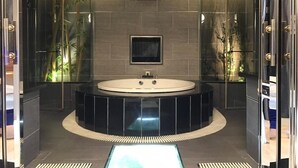 A modern bathroom with a large circular bathtub, a small mirror, and bamboo plants. - Kai-Hong Motel (Taoyuan City)